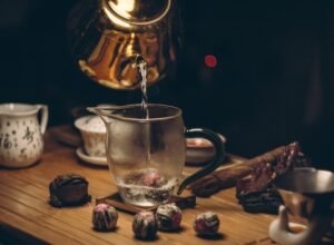 A golden teapot elegantly pours hot water into a glass pitcher on a wooden table.